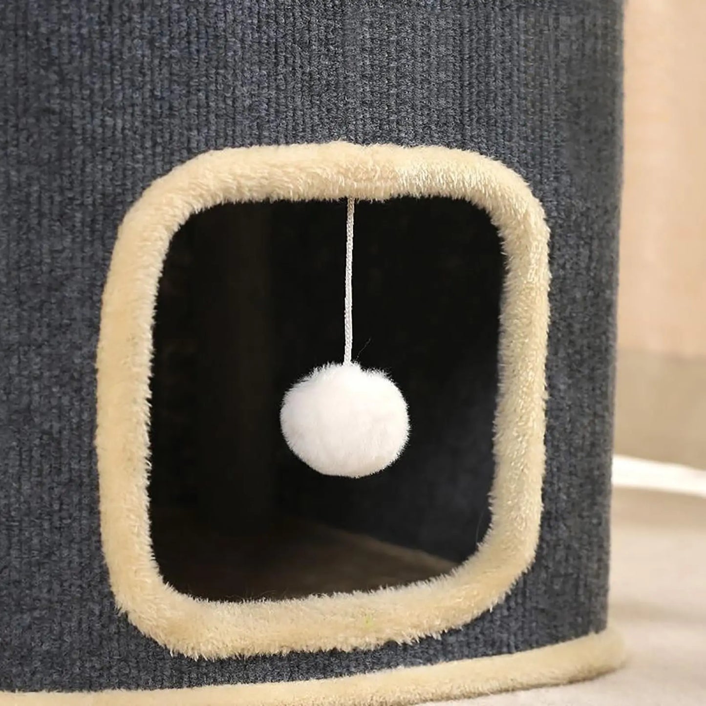 Cat tree with a white pom-pom toy hanging from a beige platform.