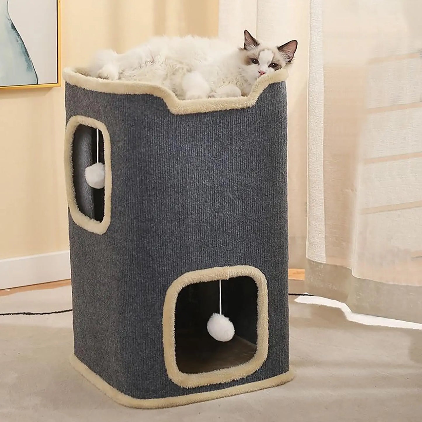 Cat sitting inside a multi-level cat tree with a ball of yarn on a light wood floor.