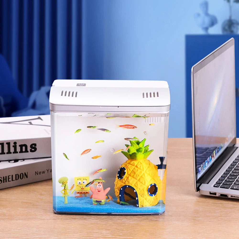 Small aquarium with pineapple-shaped house and cartoon characters on a desk with a laptop.